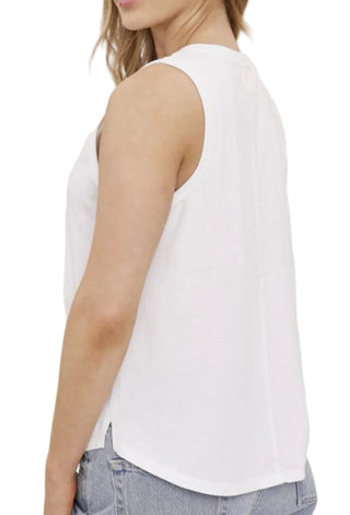 Woman wearing a white sleeveless top and blue jeans against a plain background