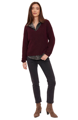 A woman modeling a dark burgundy knit sweater with a layered gray shirt underneath, paired with dark gray jeans and brown ankle boots, against a light gray studio background.