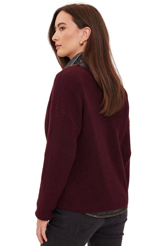 A woman shown from the back wearing a textured knit sweater in deep burgundy, paired with dark jeans and a patterned shirt collar, against a plain light background.