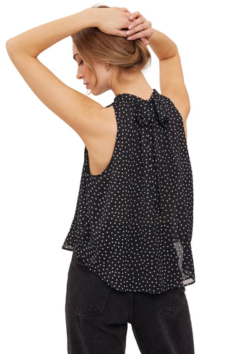 A woman wearing a black sleeveless top with a small white polka dot pattern, shown from the back against a plain light background.