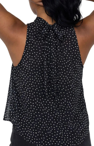 A sleeveless black top with a white polka dot pattern, shown from the back on a model with her arms raised against a light beige background.