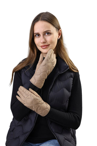 Woman wearing beige quilted gloves and a black puffer vest against a white paneled wall.