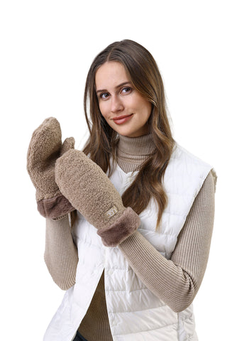 Woman wearing a white vest, beige sweater, and brown mittens against a light background