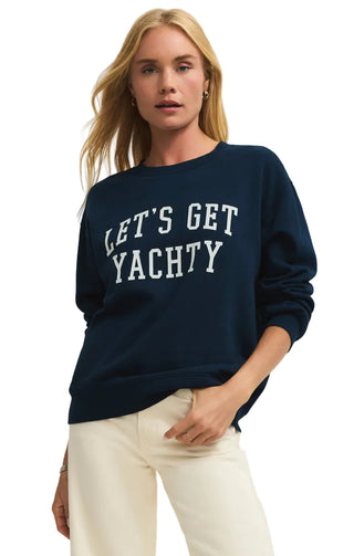 Woman wearing a navy sweatshirt with 'LET'S GET YACHTY' text on a beige background