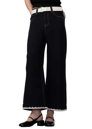 Person wearing black wide-leg jeans with a white belt on a plain background