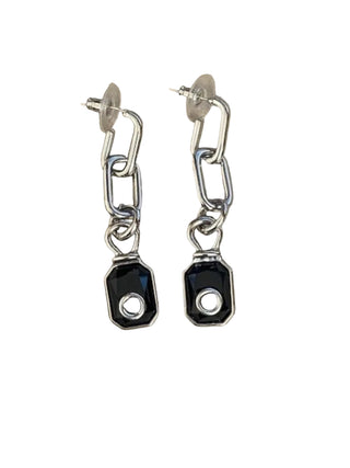 Pair of silver chain earrings with black gemstones on a beige background