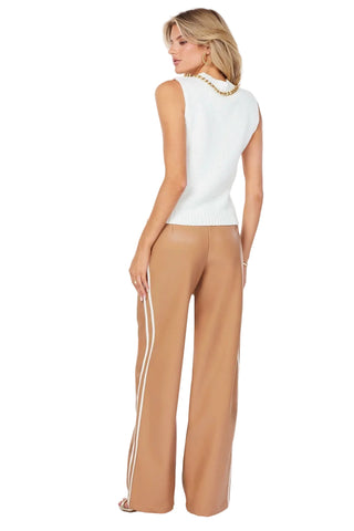 Woman wearing a white sleeveless top and tan pants with a chair in the background