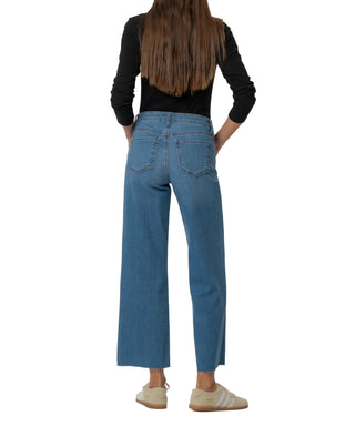 Person wearing blue jeans and a black top on a plain background