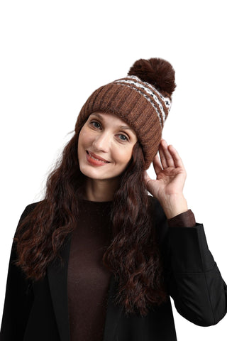 Woman wearing a brown knitted beanie with a pom-pom on a gray background