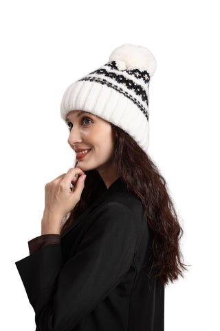 Woman wearing a white knit beanie with a black pattern and pom-pom on a light gray background