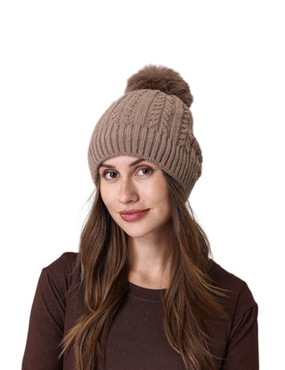 Woman wearing a brown knitted beanie with a pom-pom on a light gray background
