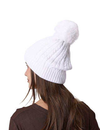 White knitted beanie with pom-pom worn by a person on a gray background