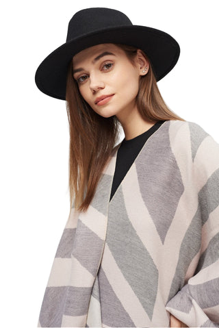 Woman wearing a black hat and a patterned shawl on a light gray background