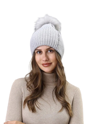 Woman wearing a white knit beanie with a pom-pom against a light background