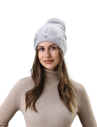 Woman wearing a white knit beanie with a pom-pom against a light gray background