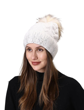Woman wearing a white knit beanie with a fluffy pom-pom on a plain background