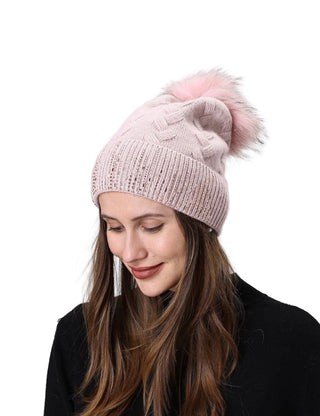 Woman wearing a pink knit beanie with a pom-pom on a light gray background