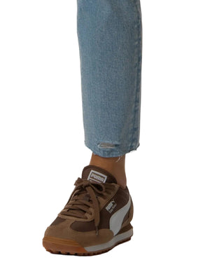 Brown Puma sneaker worn with blue jeans on a beige background