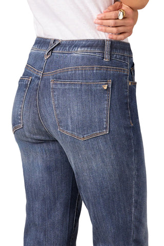 Close-up back view of a person wearing blue denim jeans with a white top, showing the back pockets and waistband against a plain beige studio background.