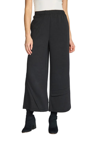 A model is shown from the waist down wearing black wide-leg cropped pants with a front crease and side pockets, paired with black ankle boots against a light gray studio background.