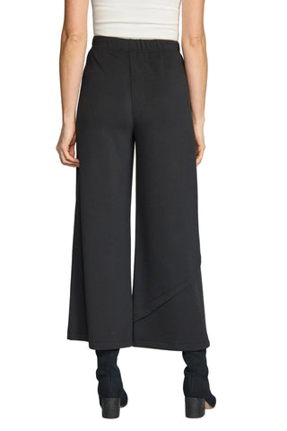 A model from the back wearing black wide-leg cropped pants, a white ribbed top, and black heeled boots against a light gray studio background.