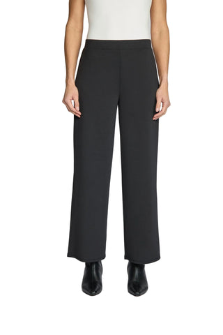 A model wearing black wide-leg cropped trousers, paired with a white sleeveless top and black pointed-toe boots, shown from the waist down against a light gray studio background.