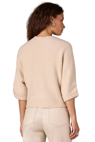 Woman wearing a beige sweater and pants against a plain background