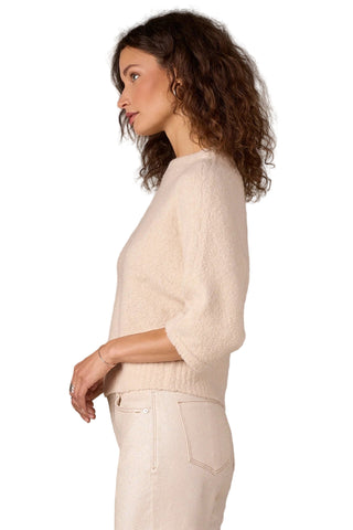 Woman wearing a light-colored sweater and pants against a beige background