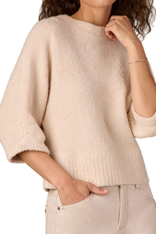 Person wearing a beige sweater and light-colored pants against a neutral background