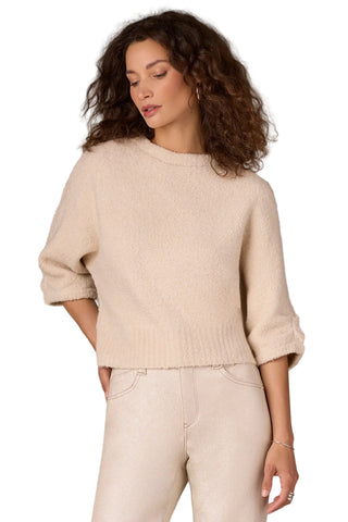 Woman wearing a beige sweater and pants against a neutral background