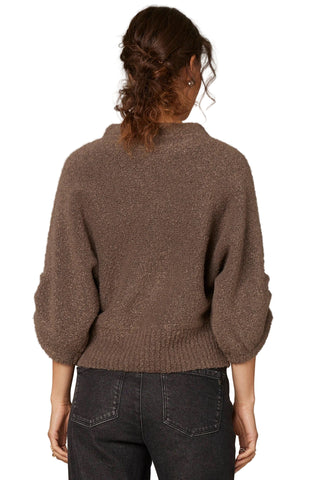 Person wearing a brown sweater and dark jeans against a plain background