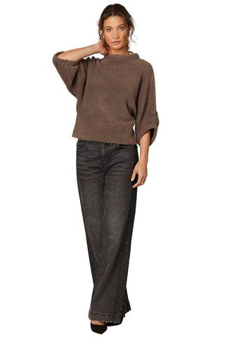 Woman wearing a brown sweater and dark jeans against a beige background