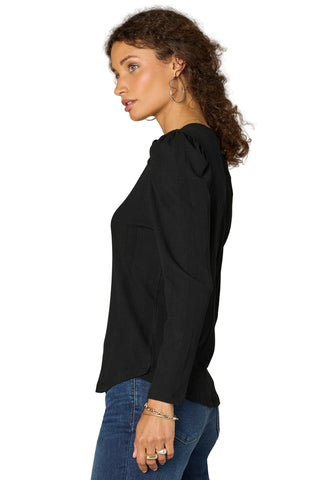 Woman wearing a black top and blue jeans against a plain background