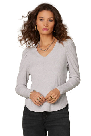 Woman wearing a light gray sweater and black pants against a beige background