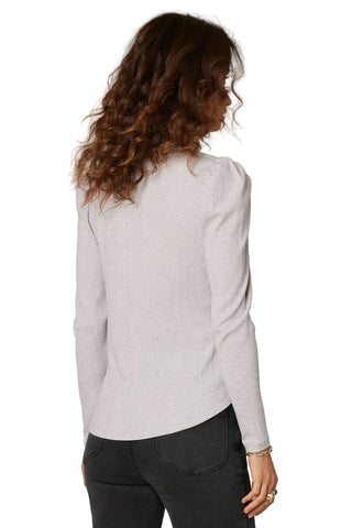 Woman wearing a light gray sweater and dark pants against a beige background
