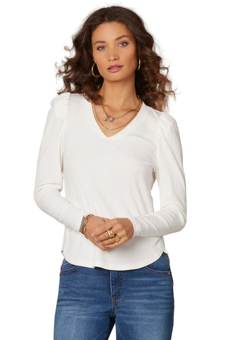 Woman wearing a white long-sleeve top and blue jeans against a beige background