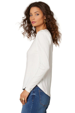 Woman wearing a white sweater and blue jeans against a beige background