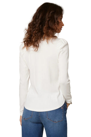 Woman wearing a white blouse and blue jeans against a beige background