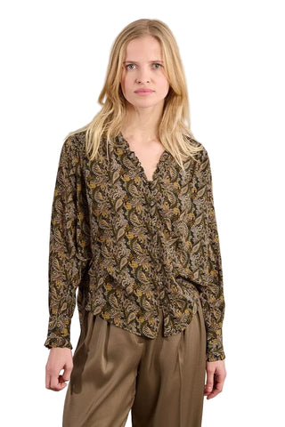 Woman wearing a patterned blouse and beige pants against a plain background