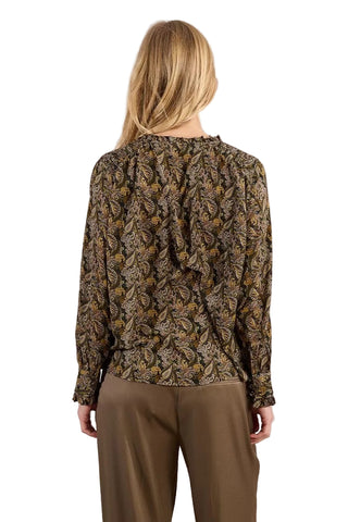 Person wearing a patterned blouse and beige pants against a plain background