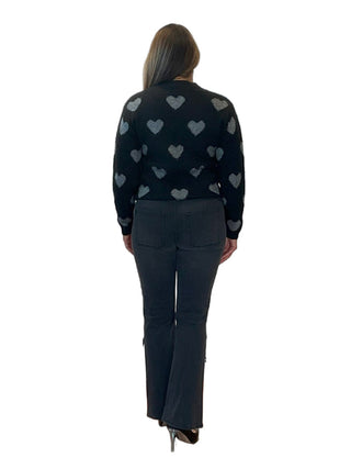 Person wearing a black sweater with heart patterns in front of an 'Anne's on the Avenue' backdrop.