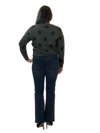 Person wearing a green star-patterned sweater and black pants in front of an 'Anne's on the Avenue' branded wall.