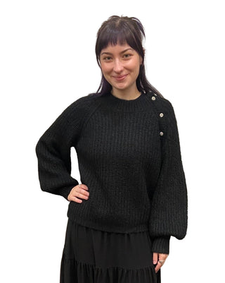 Woman wearing a black sweater with white buttons against a beige curtain background