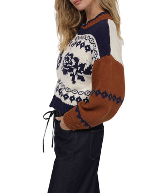 Person wearing a patterned sweater with brown and blue sleeves on a white background