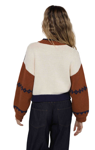 Person wearing a cream and brown sweater with blue patterns on a white background