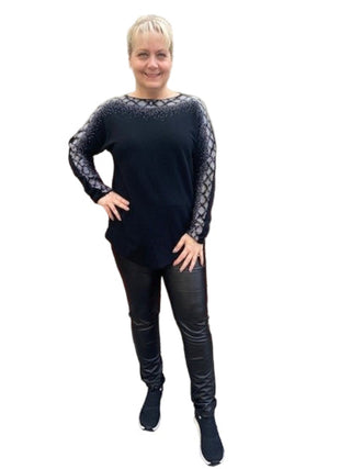 Person wearing a black outfit with patterned sleeves standing against a brick wall.