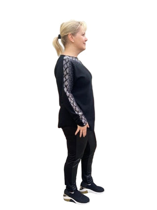 Person wearing a black outfit with lace sleeves against a brick wall.