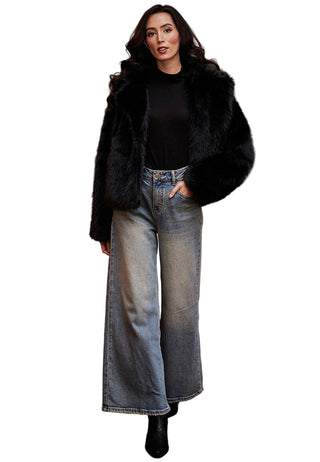 Woman in black fur coat, black top, and blue jeans standing in a room with a red sofa and classical painting.