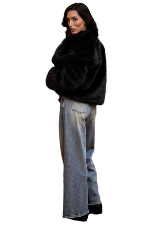 Woman wearing a black fur coat and blue jeans standing in front of a red sofa and painting.