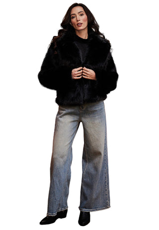 Woman wearing a black fur coat and jeans standing in front of a red sofa and painting.